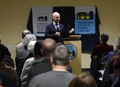 Author Jonathan Eig, wearing a suit, addresses a crowd inside Tompkins County Public Library's BorgWarner Community Center