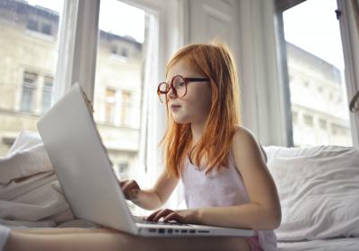 A young red-headed girl with glasses using a laptop computer.
