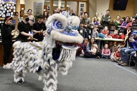 A costumed lion dances as a crowd of children and adults look on