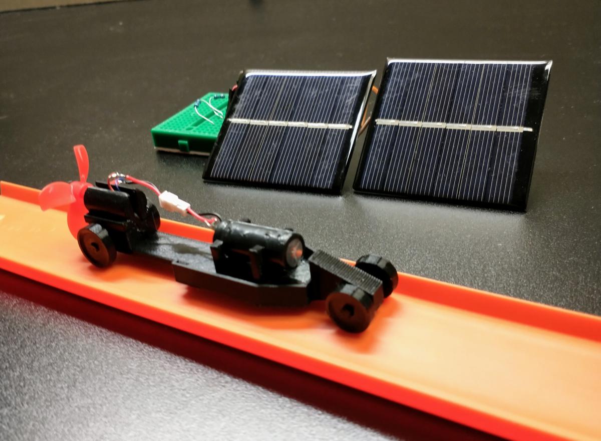 A 3D printed car on orange Hot Wheel track next to two solar cells.